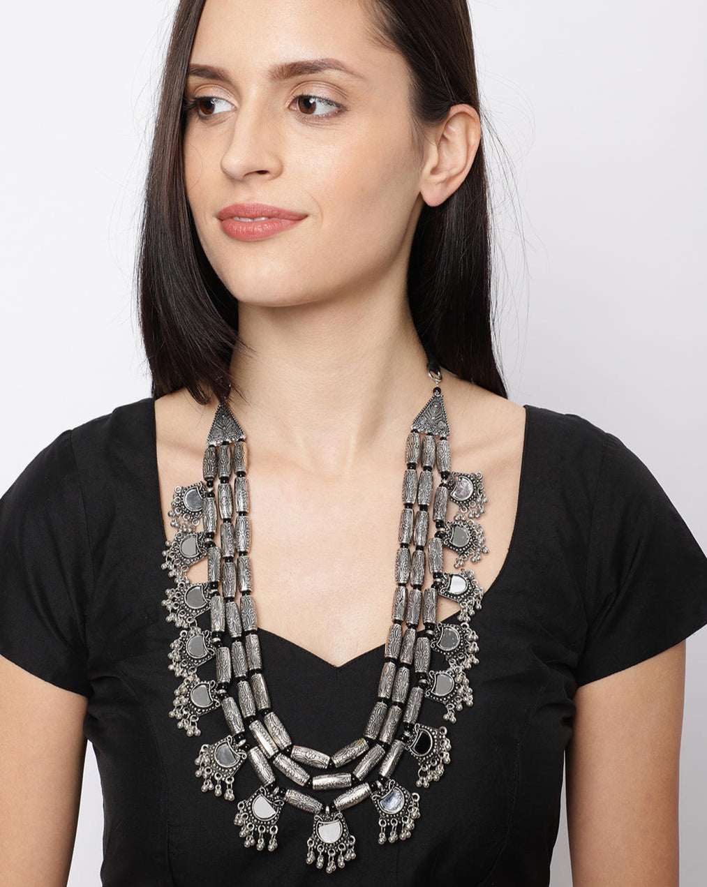 A woman wearing a black top and showcasing a multistrand long necklace with silver floral drops and intricate mirror work.