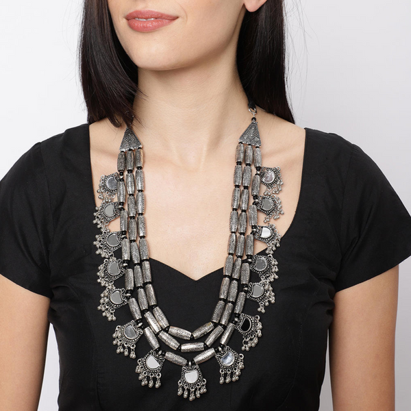 A woman wearing a black top and showcasing a multistrand long necklace with silver floral drops and intricate mirror work.