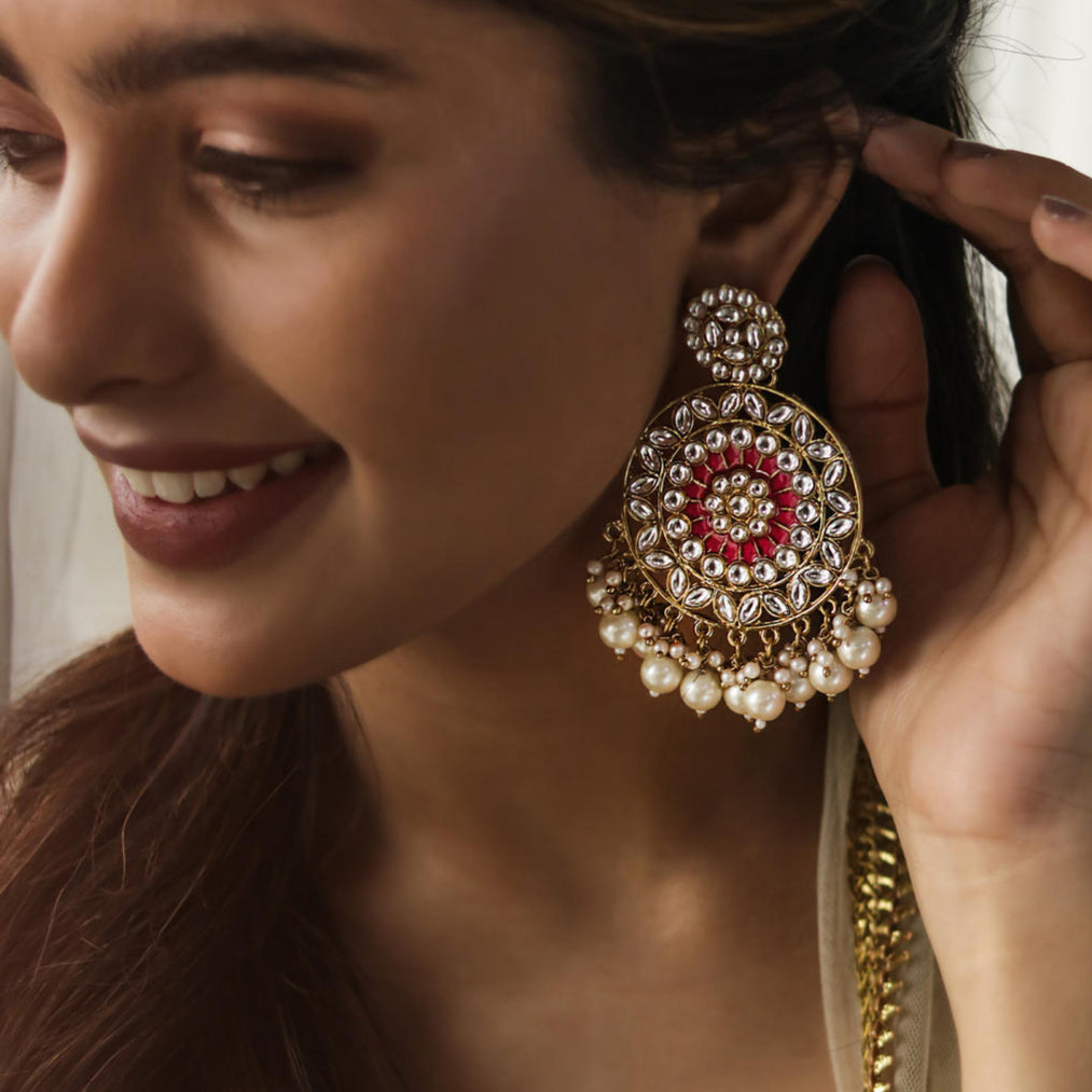 A woman wearing a gold-plated, fuchsia-colored kundan pearl jhumka earring with intricate enamel work.