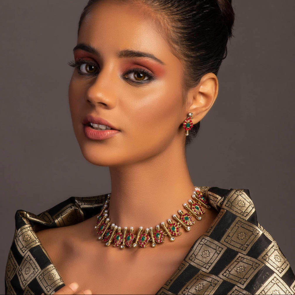 A gold plated temple jewellery set consisting of a necklace and chandbali earrings, adorned with multicolored stones and pearls.