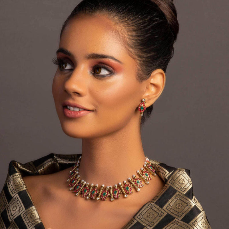 A gold plated temple jewellery set consisting of a necklace and chandbali earrings, adorned with multicoloured stones and pearls.
