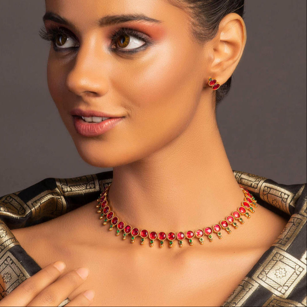 A gold-plated jewellery set with a necklace and a pair of earrings, featuring red and green embellishments