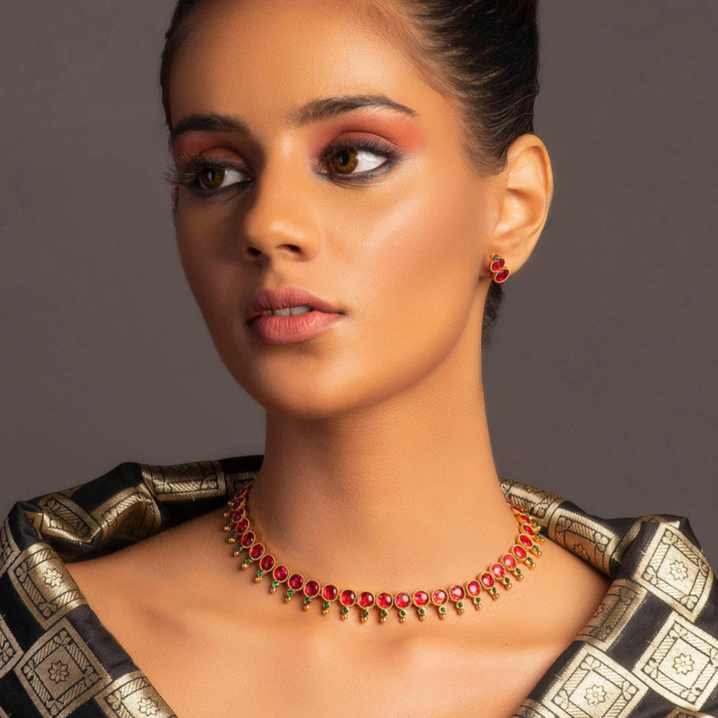 A gold-plated jewellery set with a necklace and a pair of earrings, featuring red and green embellishments