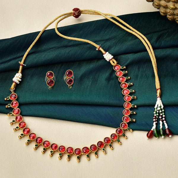 A gold-plated jewellery set with a necklace and a pair of earrings, featuring red and green embellishments, displayed on a green fabric.