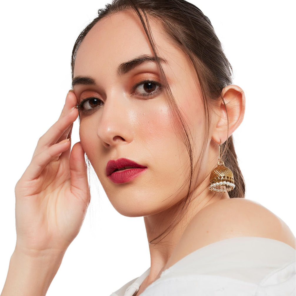A woman wearing a white off-shoulder top and gold-plated textured jhumka earrings.