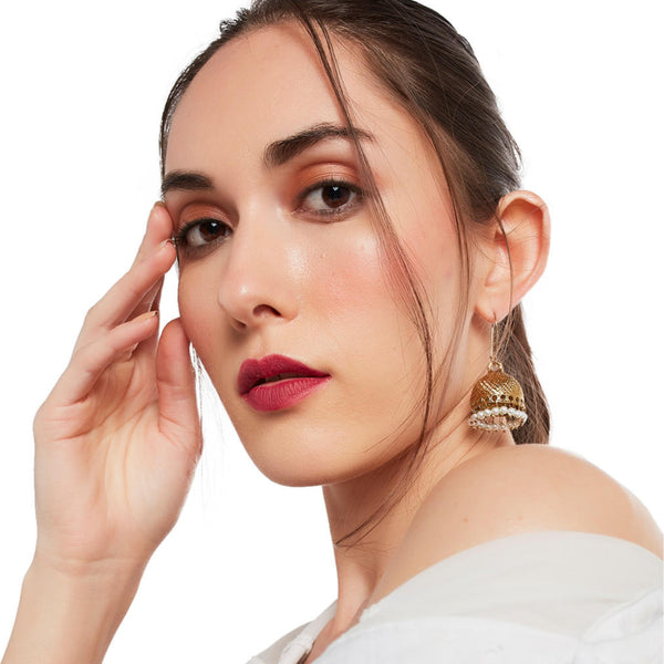A woman wearing a white off-shoulder top and gold-plated textured jhumka earrings.