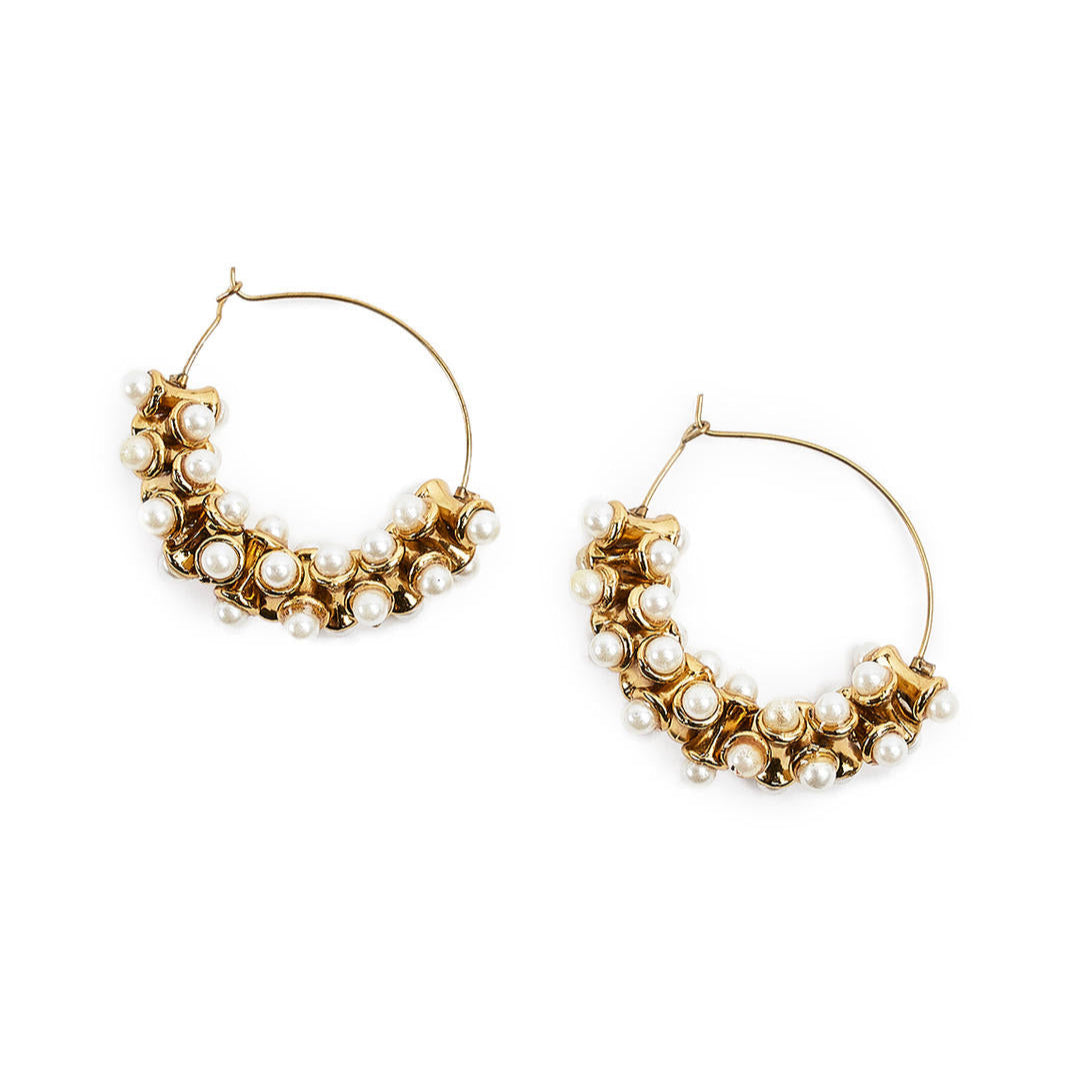 A pair of gold-plated hoop earrings adorned with white pearls, arranged in a floral pattern, on a white background.
