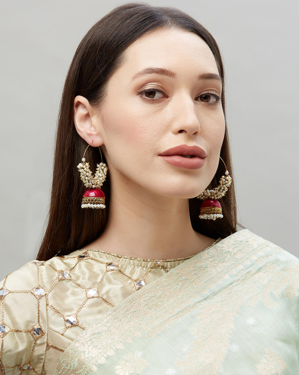 A gold-plated hoop earring with white beads and red enamel detailing
