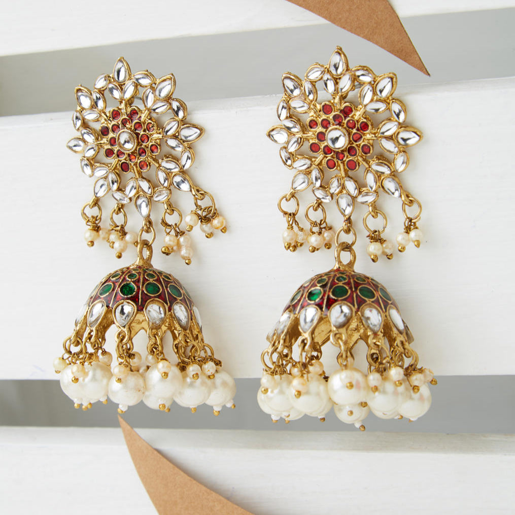 Gold plated enameled jhumka earrings with maroon kundan stones and pearl embellishments, displayed against a white background.