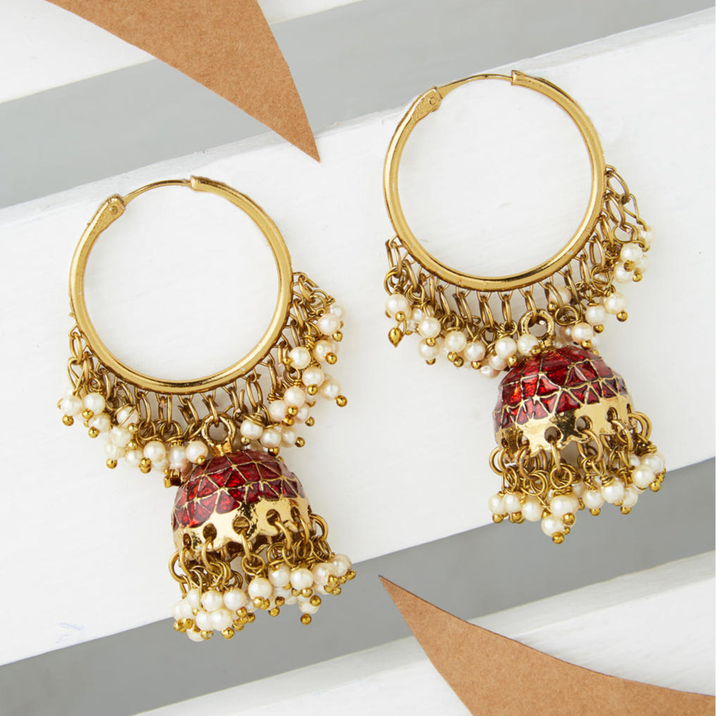A pair of gold-plated hoop jhumka earrings with red enamel and white beads embellishments, displayed against a neutral background.