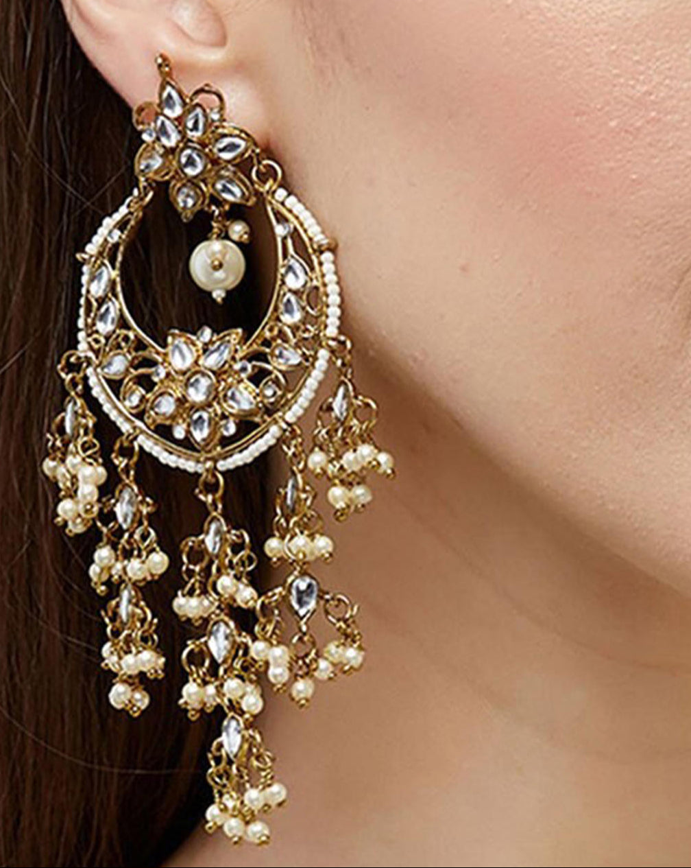 A close-up image of a woman's ear wearing a gold-plated chandbali earring embellished with kundan beads and pearls.