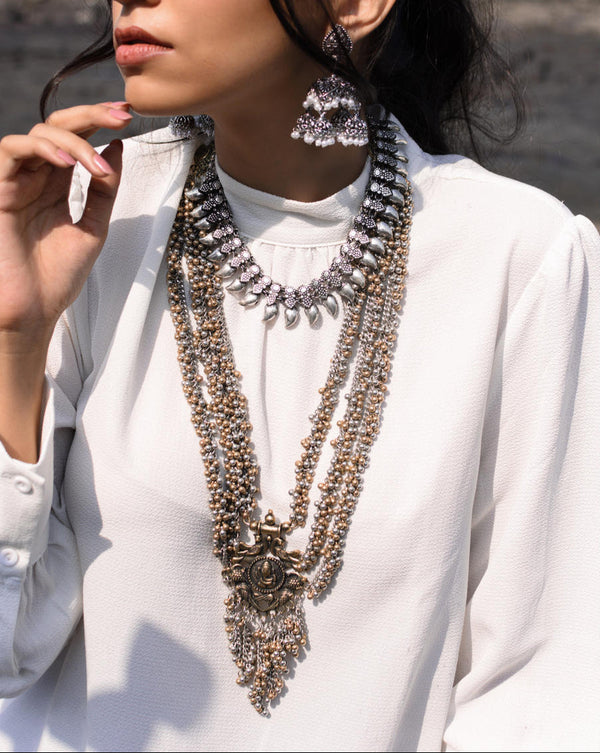 A girl wearing a multistrand long necklace with a Ganesh pendant, paired with matching earrings, in a location with an outdoor setting.