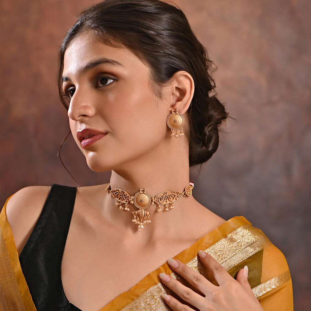 A woman wearing a gold-plated pearl choker necklace and earrings set, with intricate gold plating, in a traditional attire.