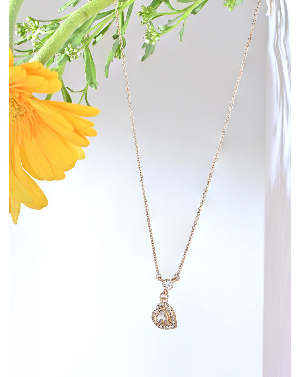 A gold-toned filigree heart pendant necklace with a central clear crystal stone, adorned with small additional stones