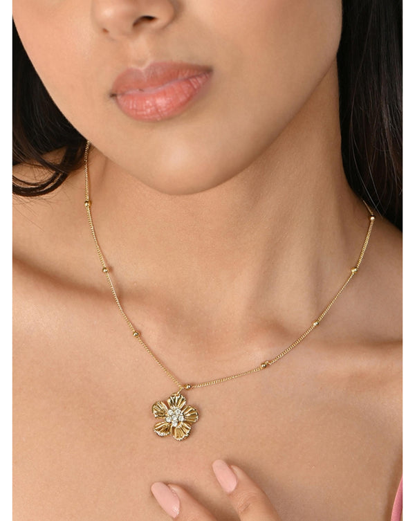 A woman wearing a gold plated floral design charm necklace with cubic zirconia stones.