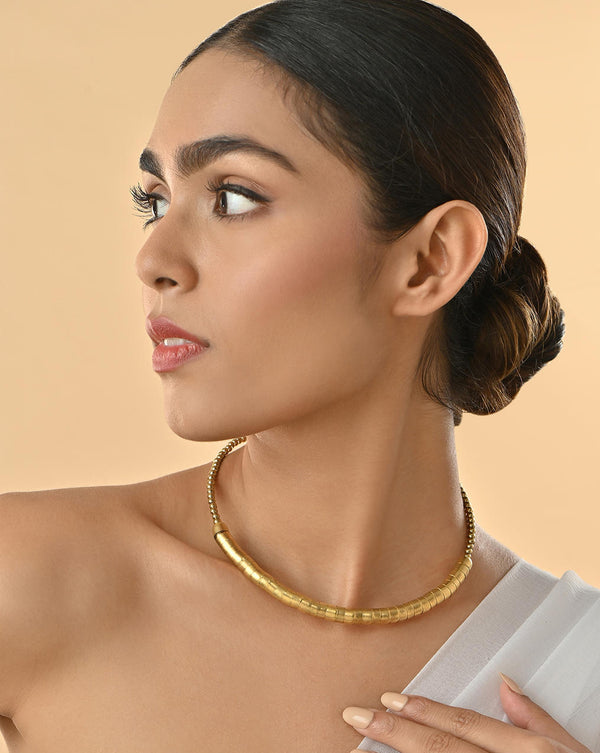 model wearing gold-toned choker necklace with a curved rod design covered in fused beads.