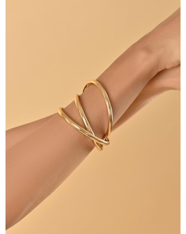 A gold-toned molten twisted shining party bracelet displayed on a person's wrist against a beige background.