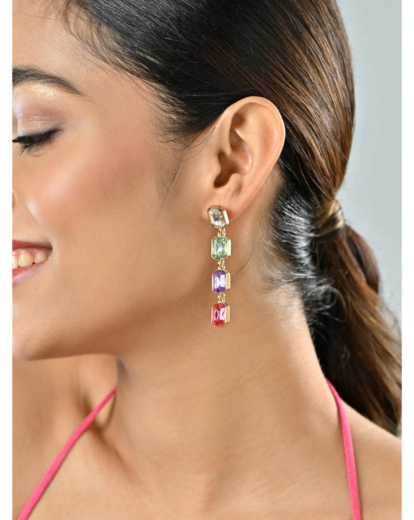 A woman wearing drop earrings with a colorful gemstone design.