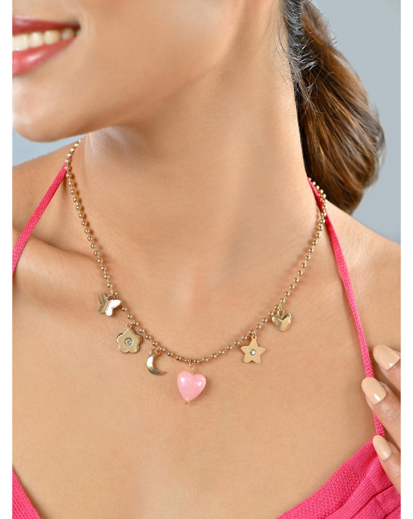 A gold-toned choker necklace with a pink heart charm and floral and moon accents, worn by a person in a pink outfit.
