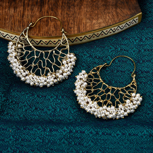 A pair of gold-plated chandbali earrings with white beads arranged in a crescent pattern, displayed on a blue textured surface.