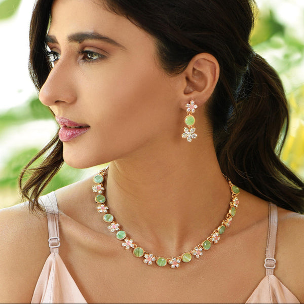 A woman wearing a gold plated floral jewellery set with pink and green stones, with matching earrings.