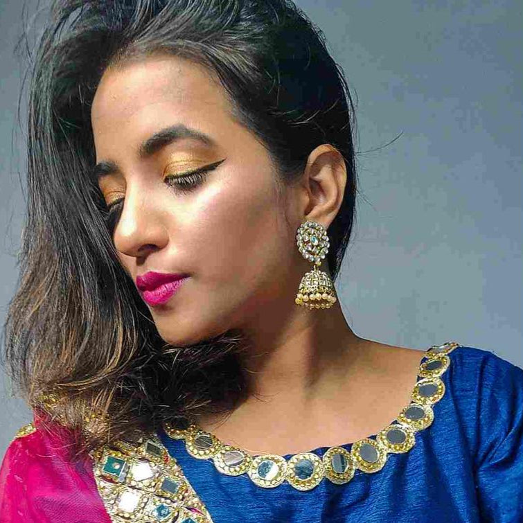 A person wearing a blue and pink traditional Indian outfit with gold-plated floral jhumka earrings.