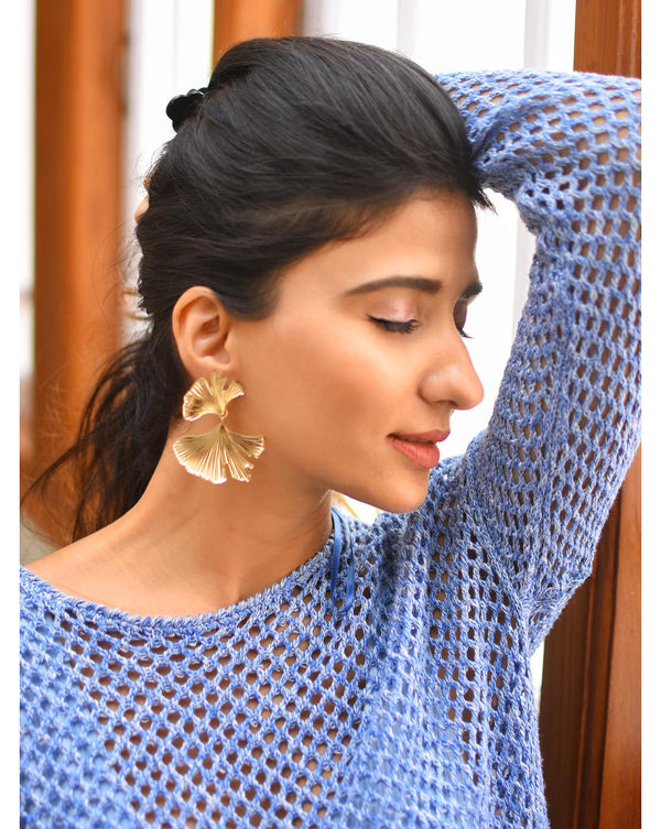 A woman wearing gold-plated floral dangle earrings and a blue mesh sweater.
