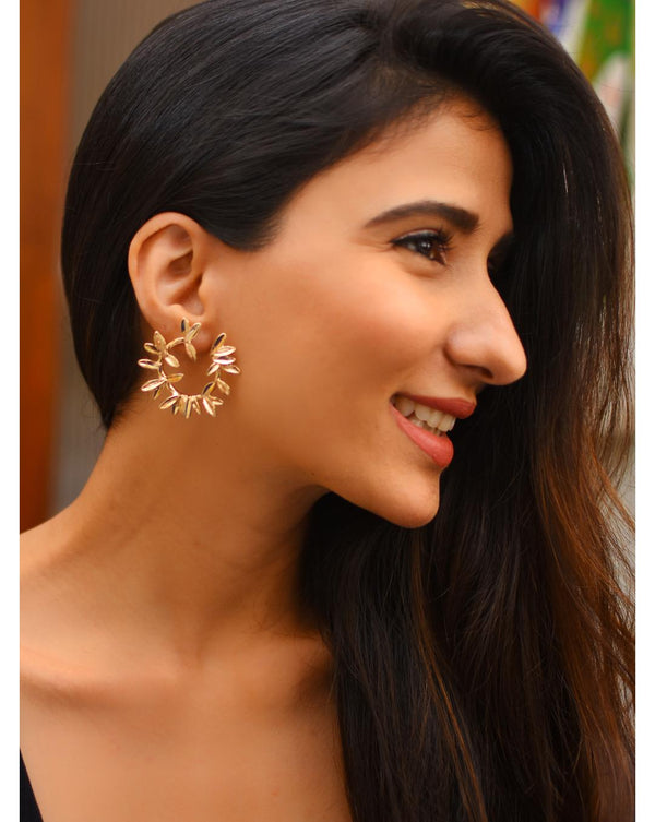A woman wearing gold-plated hoop earrings with leaf motifs.