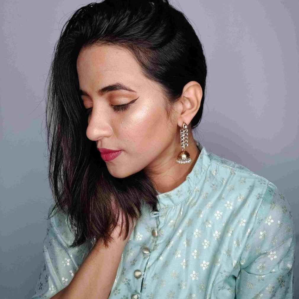 A woman wearing a traditional green salwar kameez with gold patterns, paired with a gold-plated leaf jhumka earring.